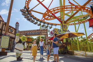 A family at Dreamworld, talking with someone dressed as Shrek, a rollercoaster behind them. Source: Destination Gold Coast